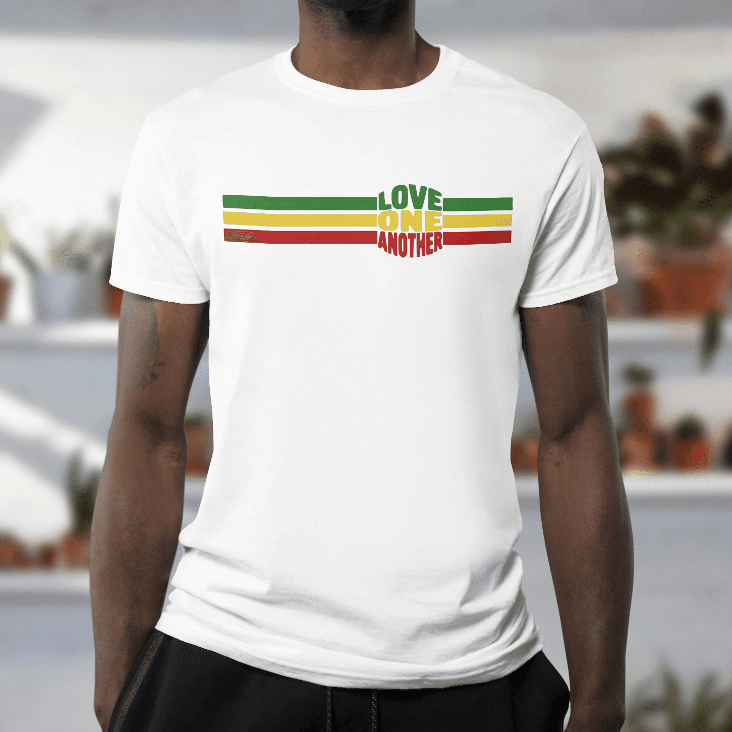 Person wearing a white t-shirt with 'Love One Another' design in Rastafarian colors.